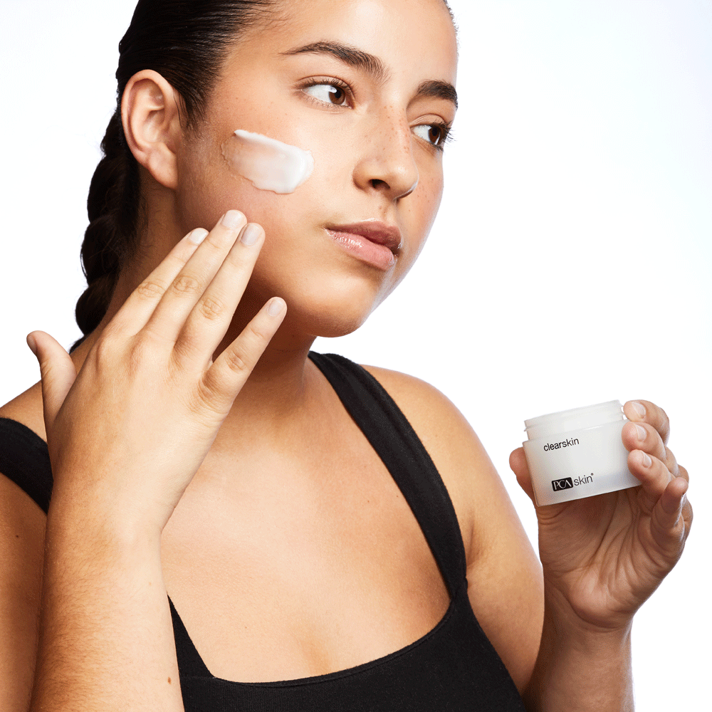 Model applying PCA Skin Clearskin to cheek while holding jar