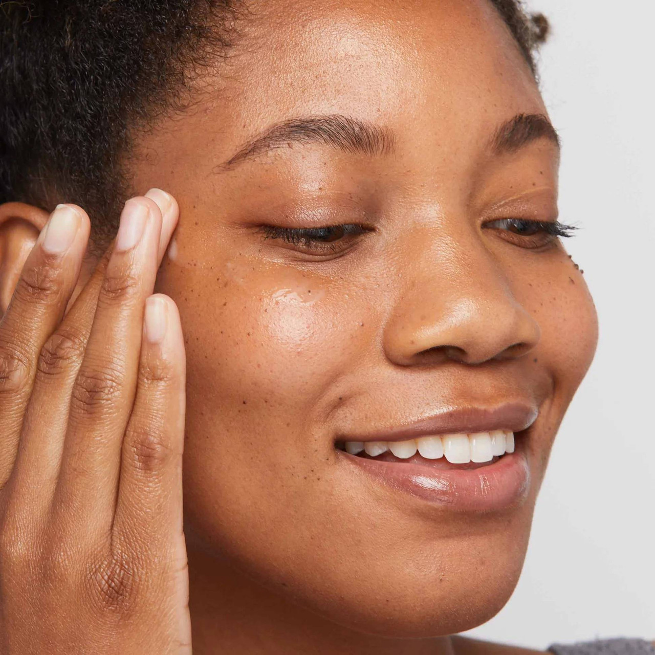 Smiling woman tapping eye serum beneath her eye