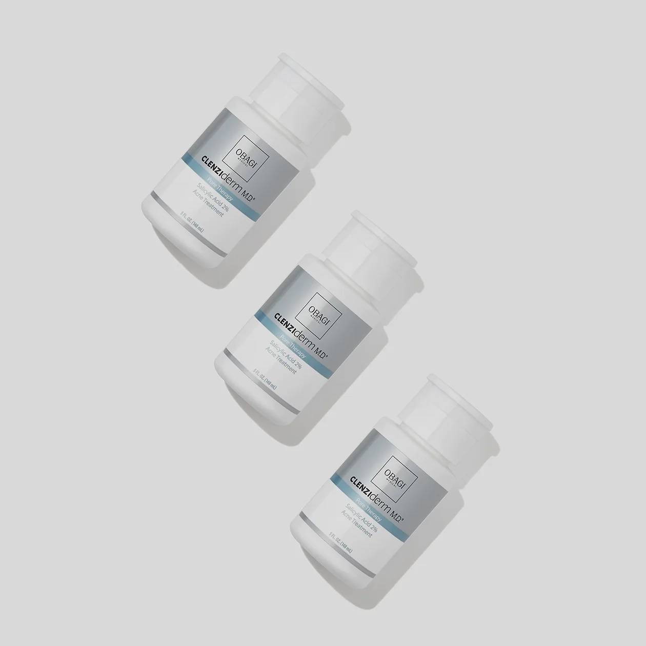 Three Obagi CLENZIderm Pore Therapy bottles on gray background