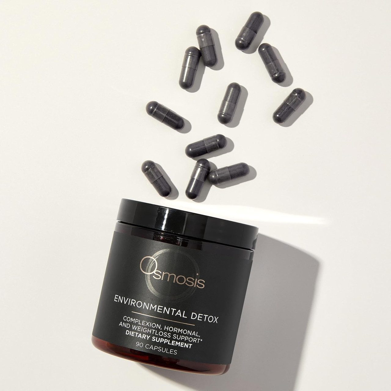 Black capsules spilling above an open Osmosis Environmental Detox jar