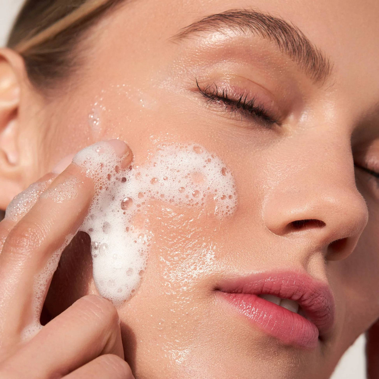 Woman with closed eyes washing her face with cleanser foam