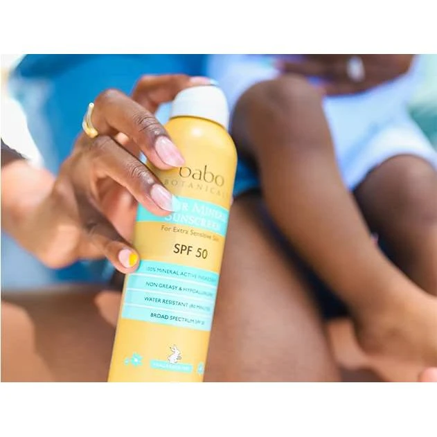 Hand holding Babo SPF 50 spray can near a child