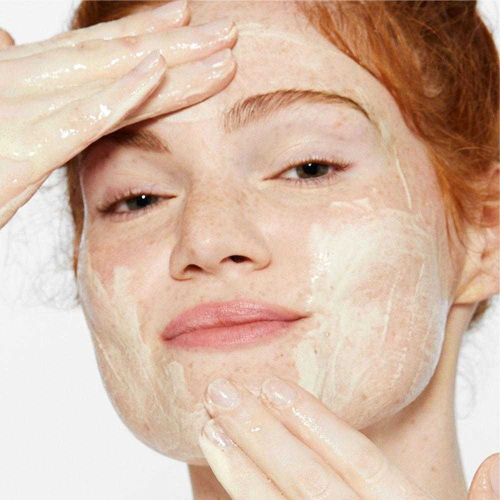 Smiling woman massaging foamy exfoliant over her forehead