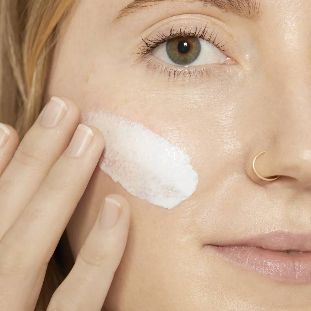 Woman applying white sunscreen to her cheek
