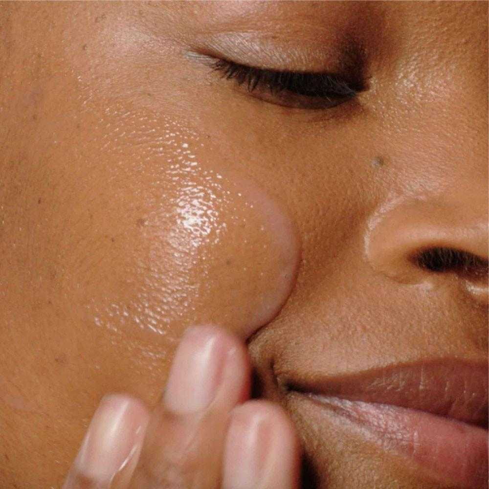 Woman applying Liquid Peelfoliant to her cheek with fingertips