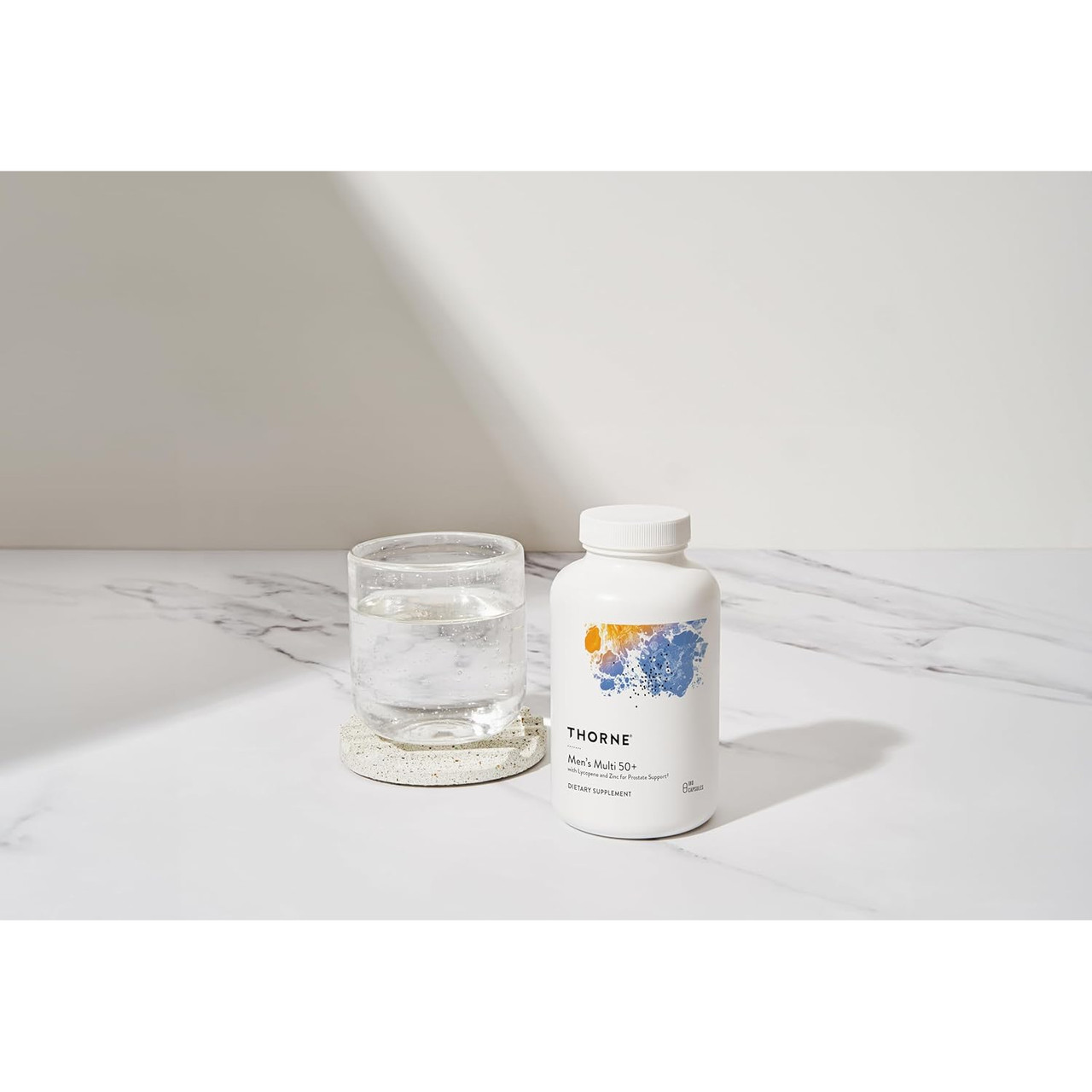 Men's Multi 50+ bottle beside a glass of water on a counter