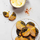 Golden milk in a cup beside sesame-coated cookies on a plate