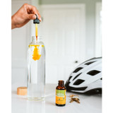 Hand adding Turmeric extract drops to a water bottle beside a bike helmet