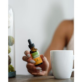 Hands holding a Herb Pharm Turmeric bottle beside a white mug
