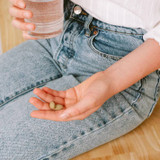 Palm holding two Kapha Digest tablets beside a glass of water