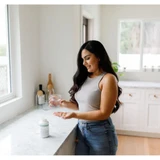 Woman in a kitchen holding a glass of water and capsules