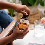 Hands opening Organic India Turmeric Formula bottle beside a glass of water