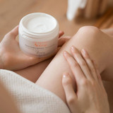Hands holding an open jar of Avène Moisturizing Melt-in Balm showing the cream texture