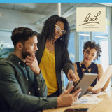 Three coworkers reviewing a tablet in an office with Bach logo