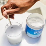 Hand stirring CALM Plus Calcium powder into glass of water lifestyle shot