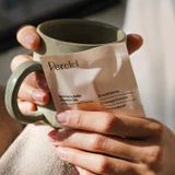 Hands holding a Perelel packet and a mug