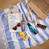 Self tan mousse on a striped beach towel with sunglasses, lemons and a straw bag
