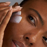 Woman applying white sunscreen to her cheek