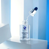 iS Clinical Youth Serum bottle with dropper raised against a blue background
