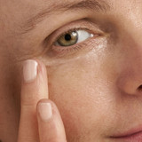 Close-up of fingertip applying eye cream under the eye