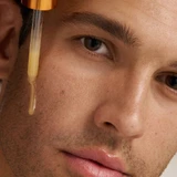Male model applying Dermalogica BioLumin-C Serum from dropper to cheek
