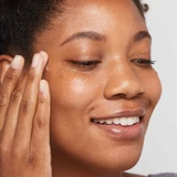 Smiling woman tapping eye serum beneath her eye