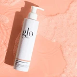 glo Skin Beauty GlyPro AHA Resurfacing Cleanser bottle on a pink water background