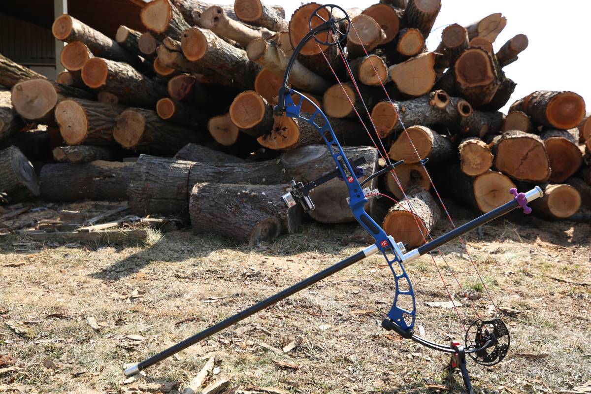A compound bow in front of a pile of wood