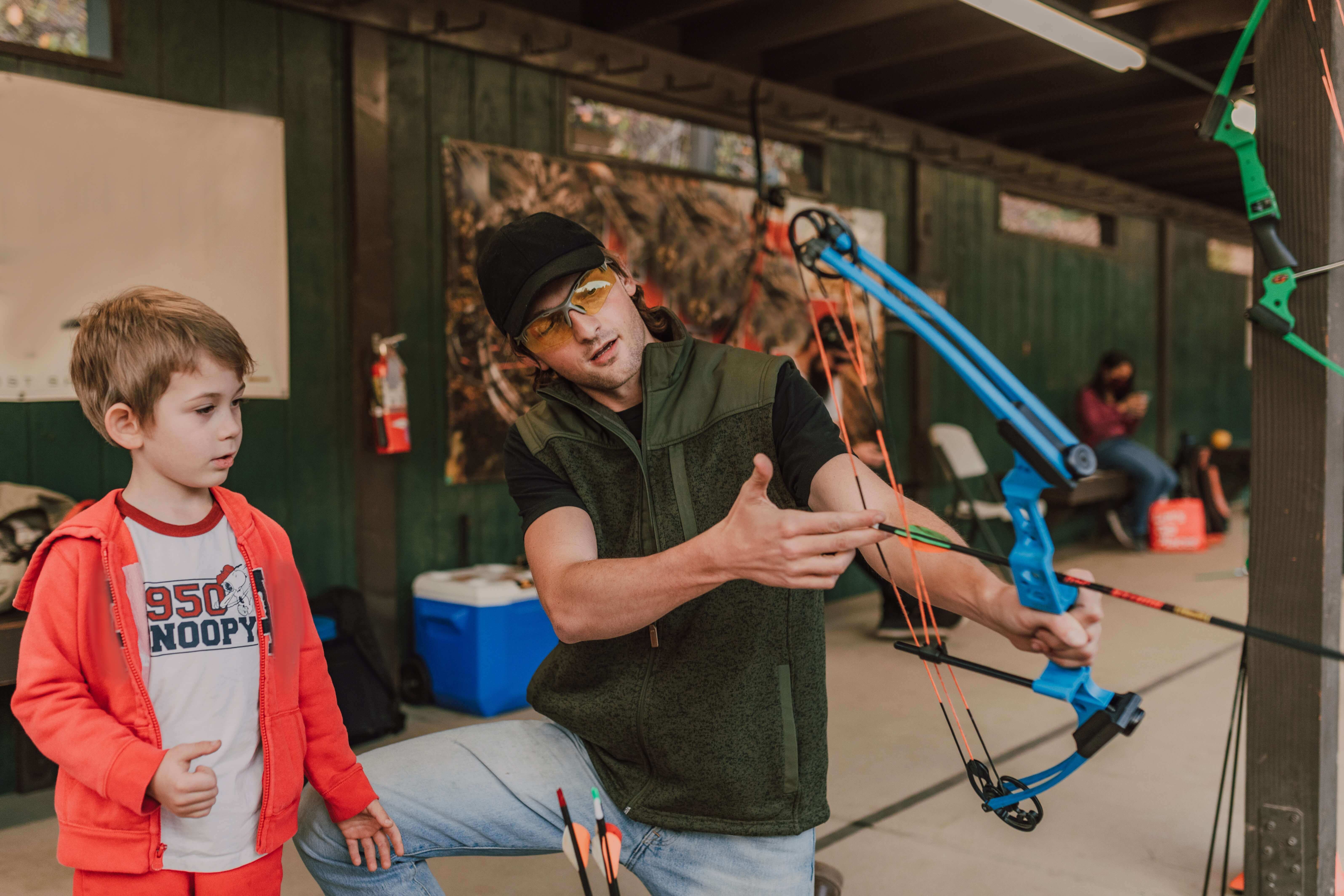 man showing a boy how to use a compound bow