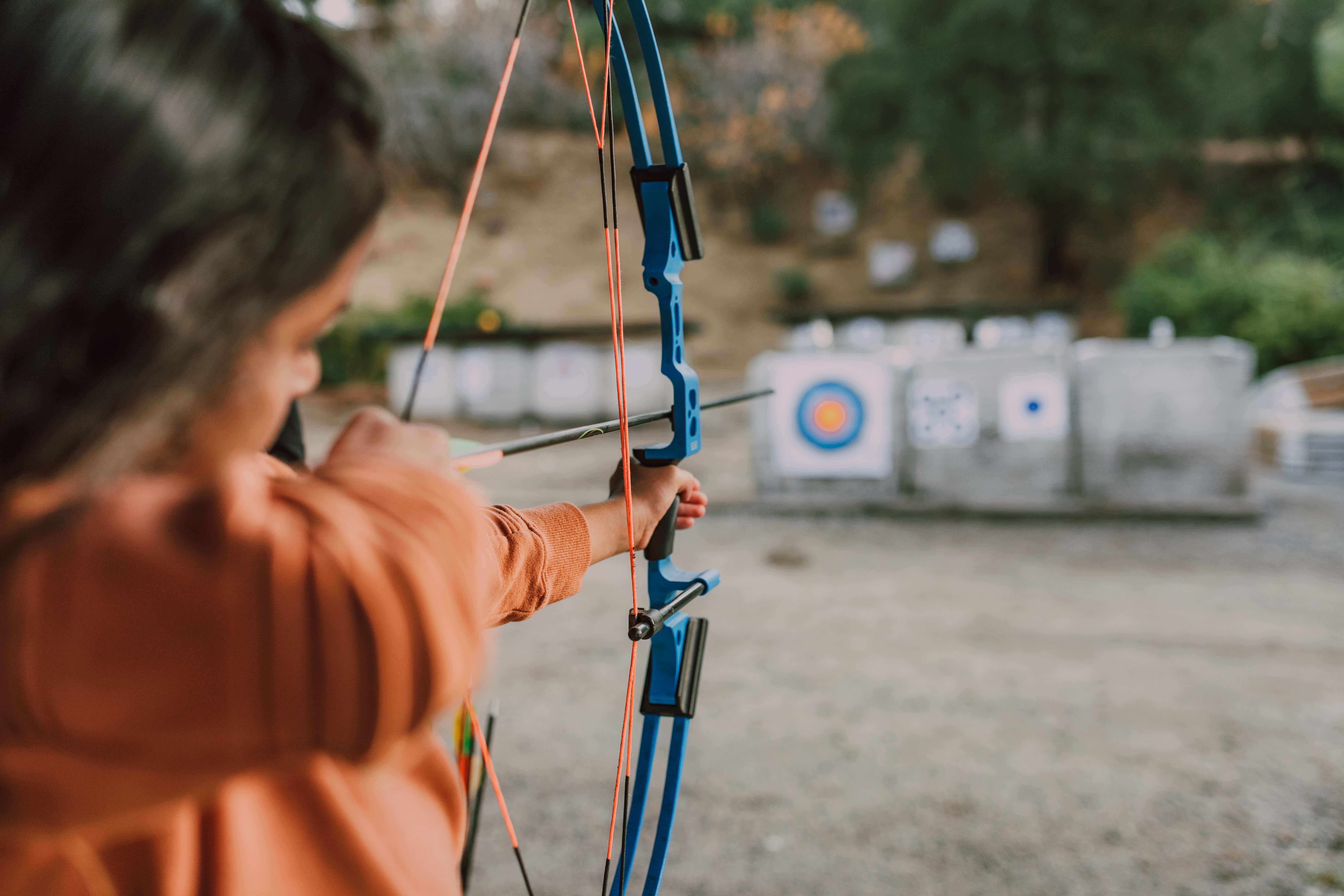 selective focus of young girl aiming compound bow at outdoor target