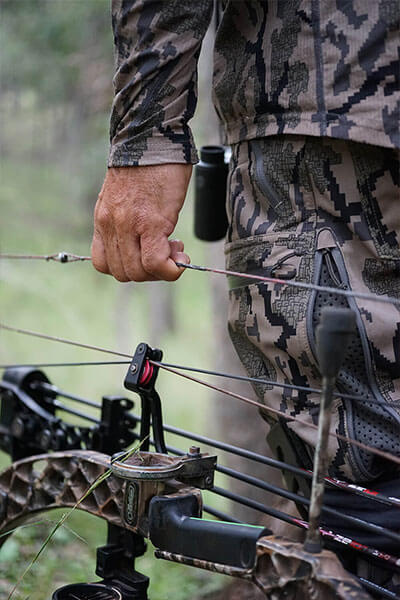 A man in a camo suit holding a bow by its bow string