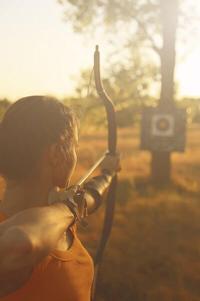 a female archer shooting an arrow at a target under the sunset