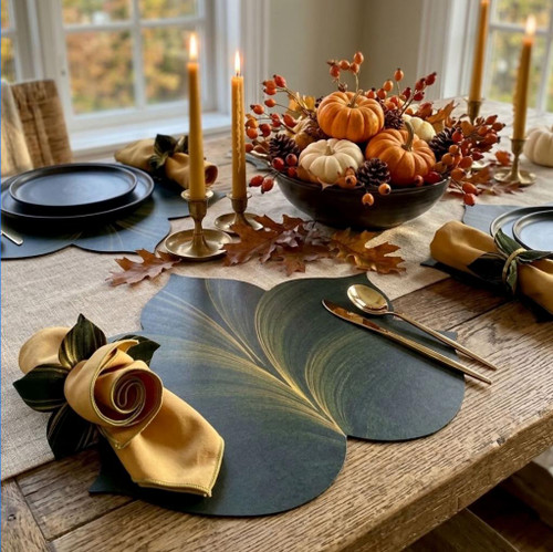 5 Point Fountain Leaf - Pine/Gold Carole Shiber Designs, a fall-themed dining table setup with a black bowl filled with mini pumpkins, autumn leaves, and berries, surrounded by candles, gold utensils, and napkins with decorative napkin rings, on sage green leaf-shaped placemats.