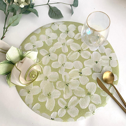 White Petals on Field of Green Carole Shiber Designs, a decorative circular tablecloth with white floral pattern on green background, accompanied by a gold spoon and knife, a glass, and a cream-colored ribbon with a green leaf, on a white surface with some greenery. White Petals on Field of Green Carole Shiber Designs, a decorative circular tablecloth with white floral pattern on green background, accompanied by a gold spoon and knife, a glass, and a cream-colored ribbon with a green leaf, on a white surface with some greenery.