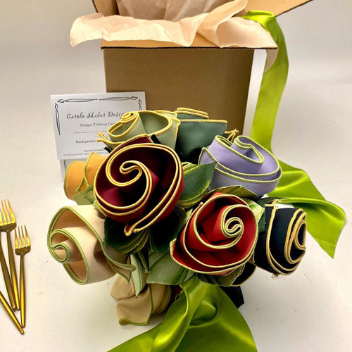 All-Season Bouquet Carole Shiber Designs, handcrafted fabric roses with colorful rolled petals and green leaves, arranged in a bouquet with a green ribbon and a cardboard box in the background. All-Season Bouquet Carole Shiber Designs, handcrafted fabric roses with colorful rolled petals and green leaves, arranged in a bouquet with a green ribbon and a cardboard box in the background.