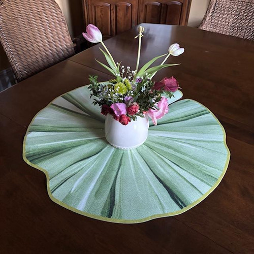 Painterly Lilypad Centerpiece Carole Shiber Designs, a floral arrangement in a white vase on a green lily pad-themed table mat, displayed on a wooden dining table. Painterly Lilypad Centerpiece Carole Shiber Designs, a floral arrangement in a white vase on a green lily pad-themed table mat, displayed on a wooden dining table.