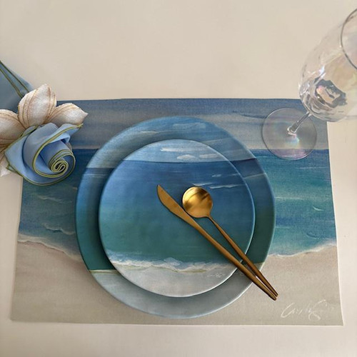 Shoreline Dining Duet, elegant table setting with ocean-themed plates, gold utensil set, wine glass, and floral napkin on a beach-inspired placemat.