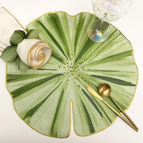 ARTPrints Botanic Round Placemat, Sage, designed by Carole Shiber, with a green leaf pattern, a gold spoon and knife, a wine glass, and a white napkin with a gold trim, displayed on a white surface.