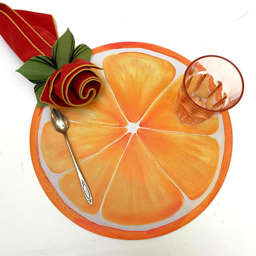 Add a Orange Slice Placemat Carole Shiber Designs, round orange-themed placemat resembling orange slices with a glass of water and a folded cloth napkin with faux-flower embellishment.