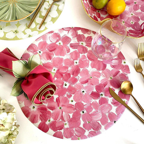 Add a Pink Petals on Round Placemat Carole Shiber Designs, pink floral painted round placemat with a glass, gold cutlery, and a pink napkin with green accents, on a table setting.