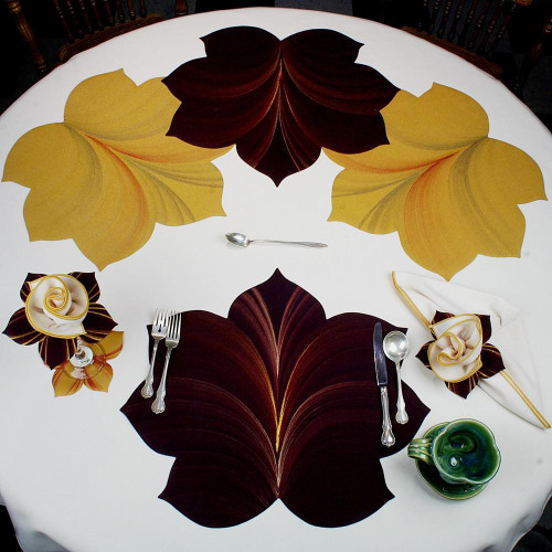 7 Point Leaf - Eggplant/Gold & Bronze Carole Shiber Designs, decorative tablecloth with leaf patterns, set with silverware, cloth napkins, and a small green decorative bowl.