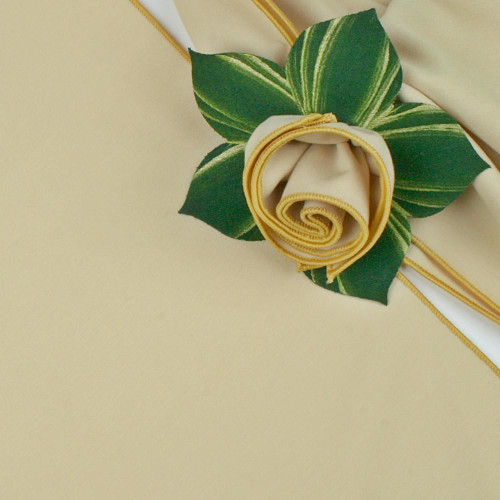 Add a Diane Wheat with Gold Trim Napkin Carole Shiber Designs, elegant cream-colored napkin with gold trim folded into a rose shape, decorated with green and gold leaves.