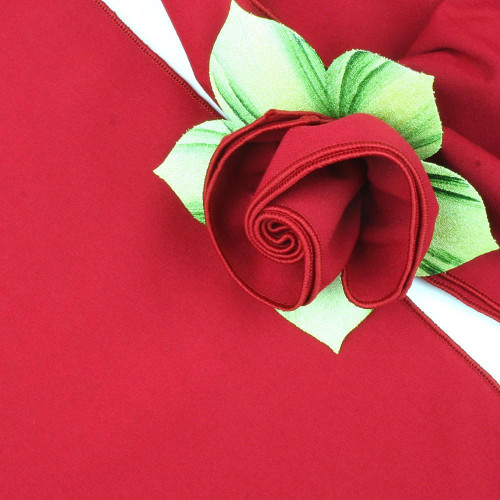 Add a Red with Red Trim Napkin Carole Shiber Designs, an image of a neatly folded red napkin with red trim, artistically folded and placed on a matching red tablecloth with green leaf accents for decorative presentation.