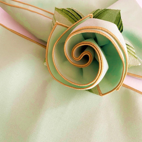 Add a Seafoam with Gold Trim Napkin Carole Shiber Designs, close-up of a decorative napkin featuring a spiral rose design with green and white sections, accented with gold trim.