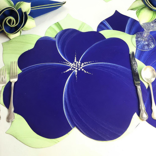 Buttercup Placemat - Dark Blue, a vibrant and artistic dark blue placemat with a white starburst design, laid on a dining table with silverware and glassware.