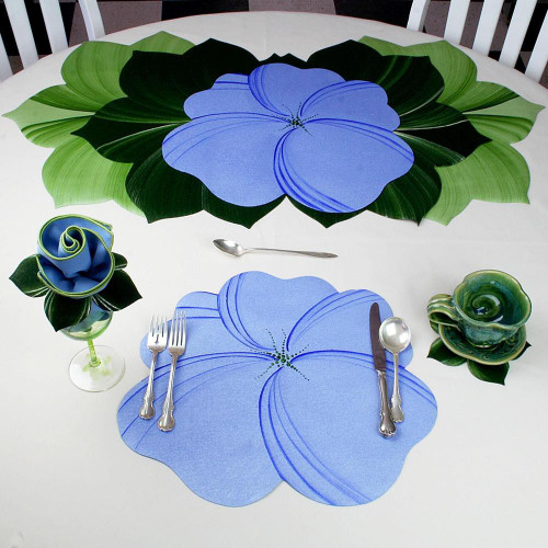 Buttercup Placemat - Light Blue Carole Shiber Designs, a blue floral placemat with leaf accents on a white table setting with matching utensils, a decorative napkin wrapped in a napkin ring, and colorful glassware.