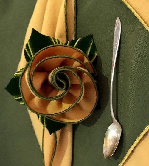Custom Napkins Builder Carole Shiber Designs, image of fabric napkins arranged in a spiral flower shape with a silver spoon on a dark and beige surface.