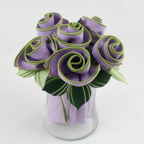 The Pure Lilac Napkin Bouquet Carole Shiber Designs, a crafted artificial bouquet of lilac-colored napkin roses with green fabric leaves in a clear glass vase. The Pure Lilac Napkin Bouquet Carole Shiber Designs, a crafted artificial bouquet of lilac-colored napkin roses with green fabric leaves in a clear glass vase.