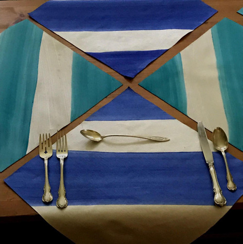 Squares 'n Stripes Set of 4 Carole Shiber Designs, colorful napkin set featuring square and stripe patterns in shades of blue, teal, white, and cream, laid out on a wooden table with silver vintage cutlery.