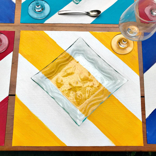 Nautical Stripes - Yellow Carole Shiber Designs, colorful table setting with yellow, white, blue, and red striped placemats, a glass wine glass, and a square glass dish on a wooden table.